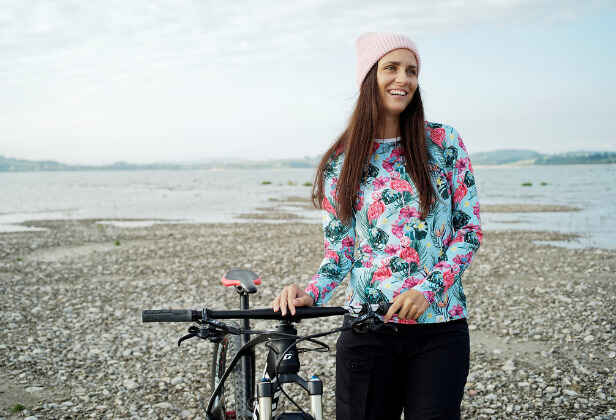 usmívající se žena v květovaném tričku na pláži, opírající se o kolo