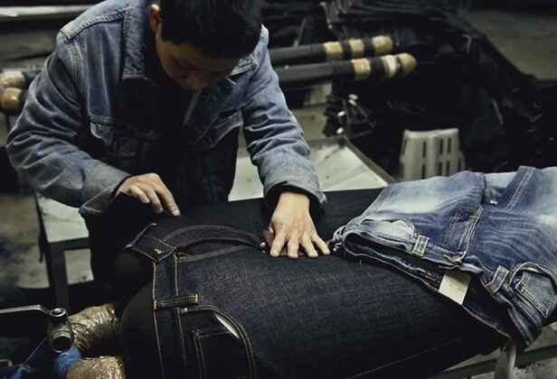 muž ve fabrice upravující povrch džín