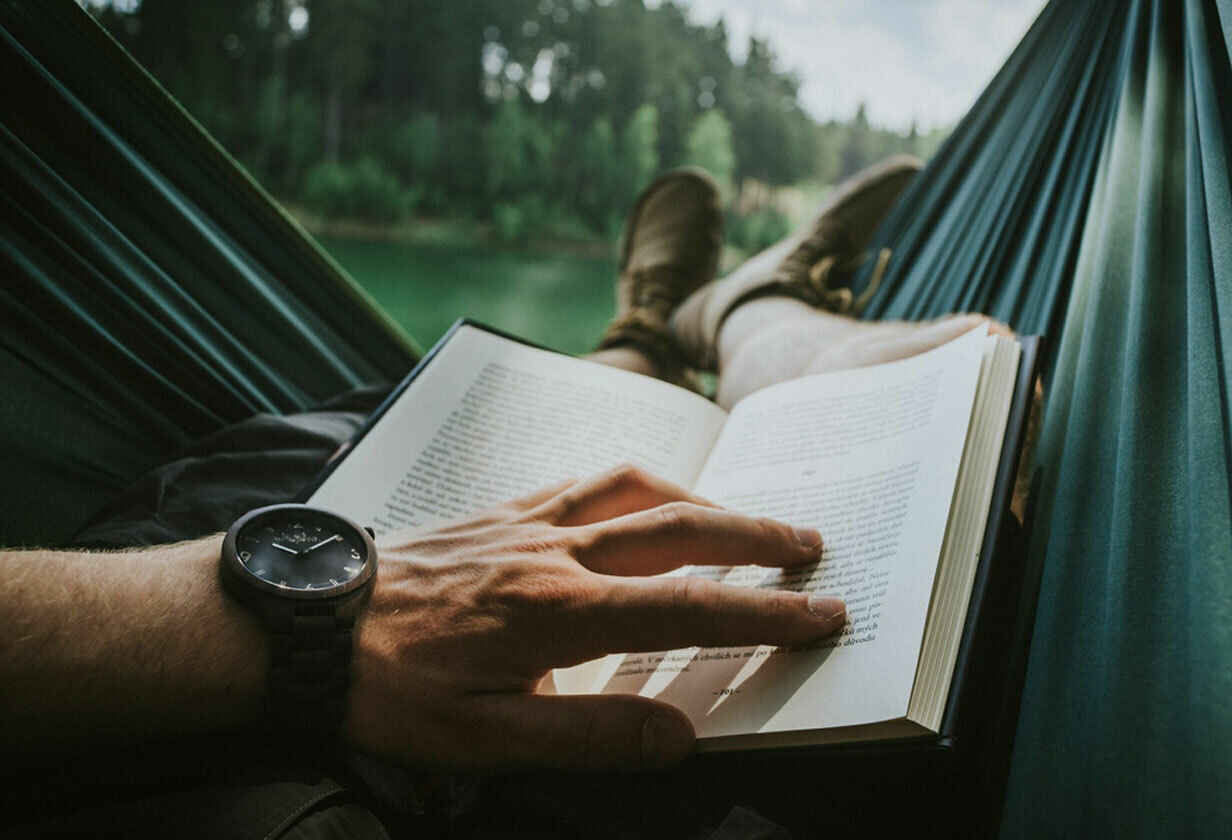 muž čtející knihu v hamace s výhledem do přírody