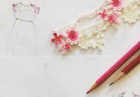návrh šatů nakreslený na papíře a detail květinové krajky