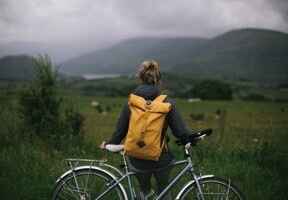 žena opřená o kolo s žlutým batohem na zádech