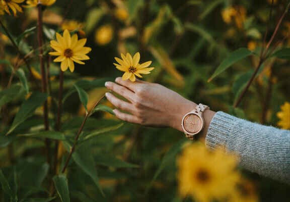 ruka ženy s hodinkami dotýkající se květin
