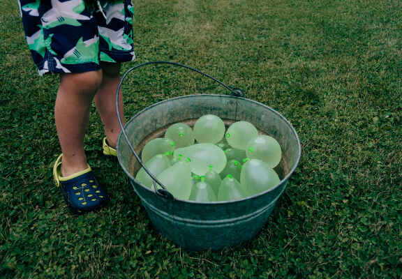 dítě s botami crocs a kyblíkem balonků naplněných vodou