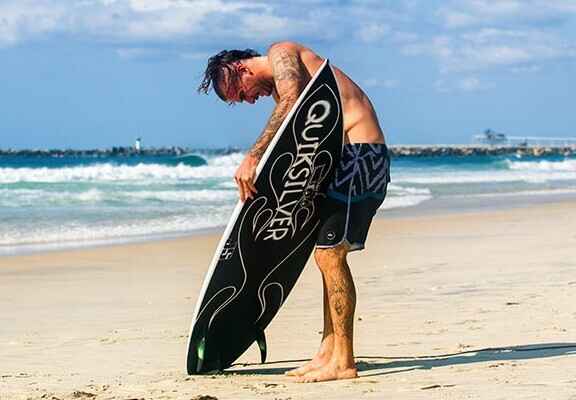 muž na pláži připravující surfové prkno