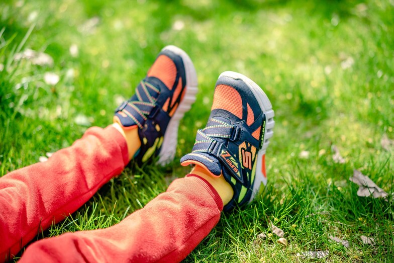 dítě ve sportovních botách sedící na trávníku